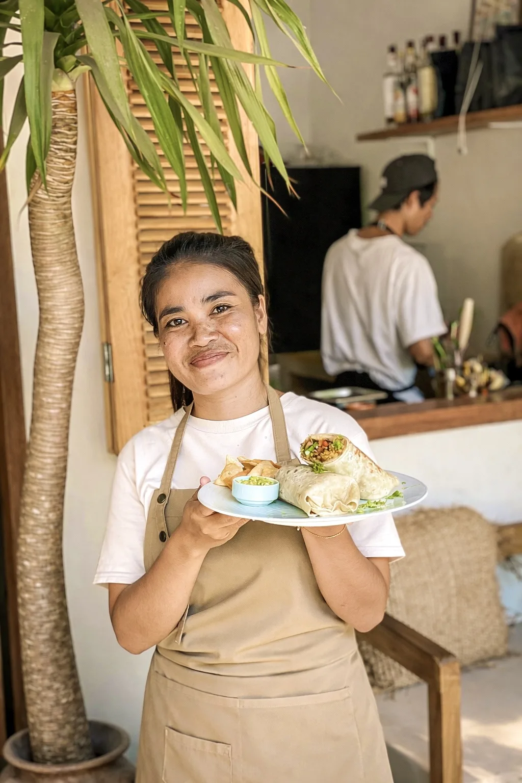 A member of the Luana Bowls team serving a plate of wraps and dumplings