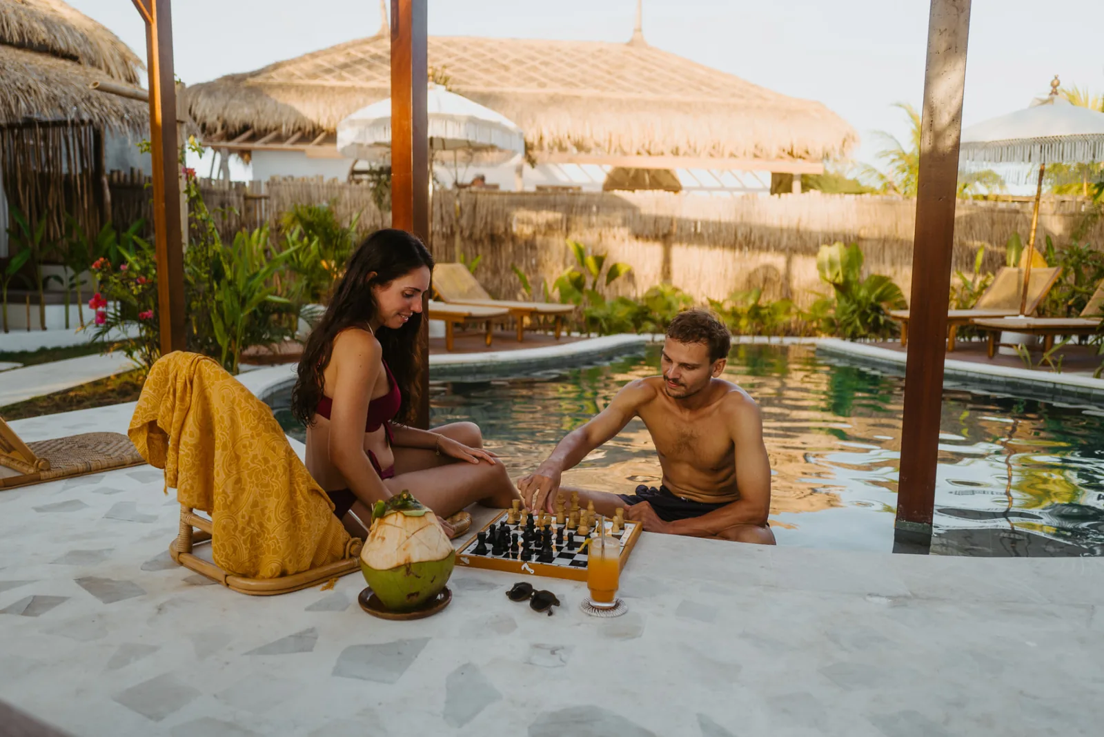 Guests playing chess by the pool in the shaded lounge area at Luana Lombok