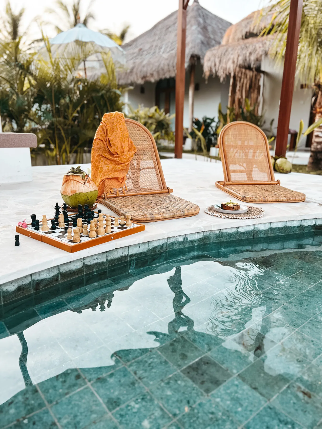 Rattan loungers, a chess board and a fresh coconut beside the pool at Luana Lombok